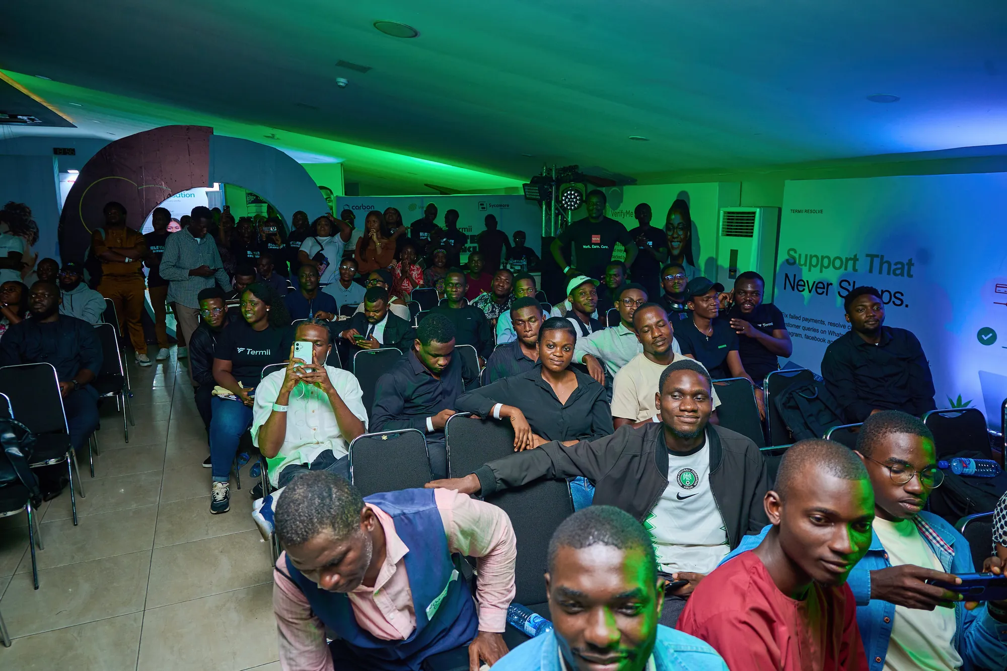 A full audience seated at the event under green stage light